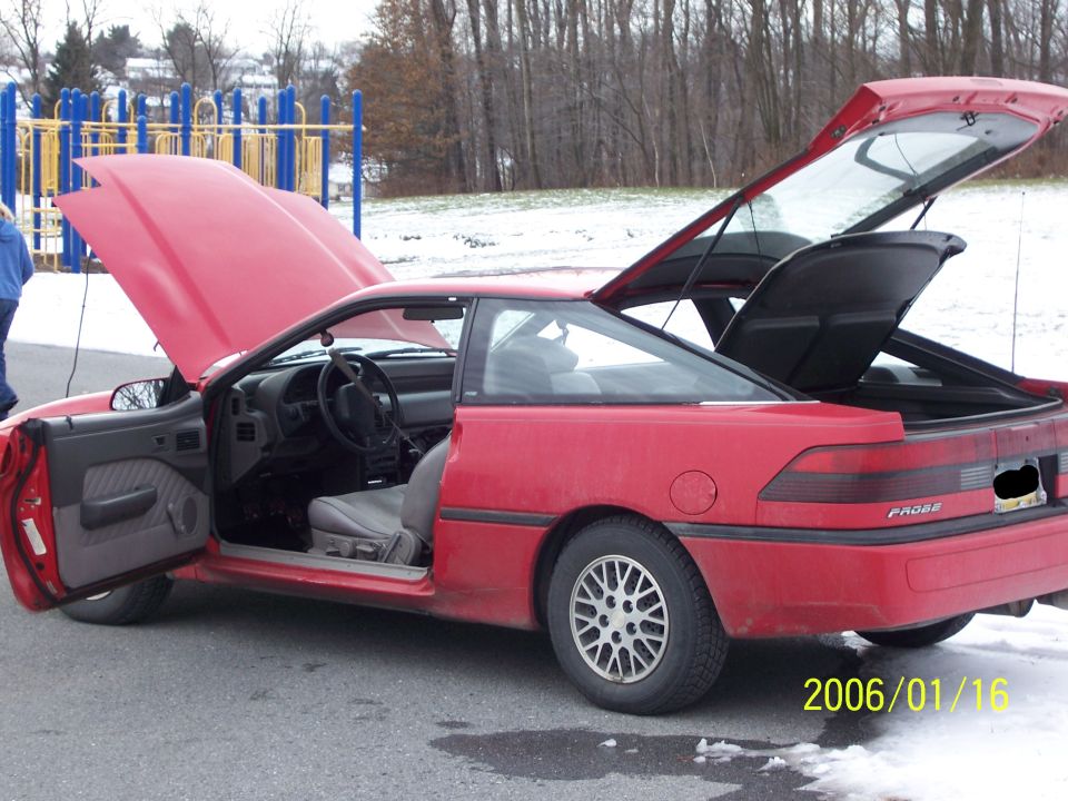 Red Ford Probe coupe doors hood and hatch all open near a playground in snow
