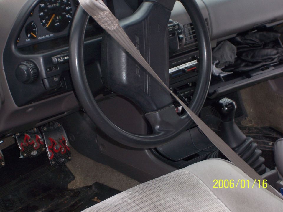Interior steering wheel, gauge cluster and manual shifter of an older car with seat belt across
