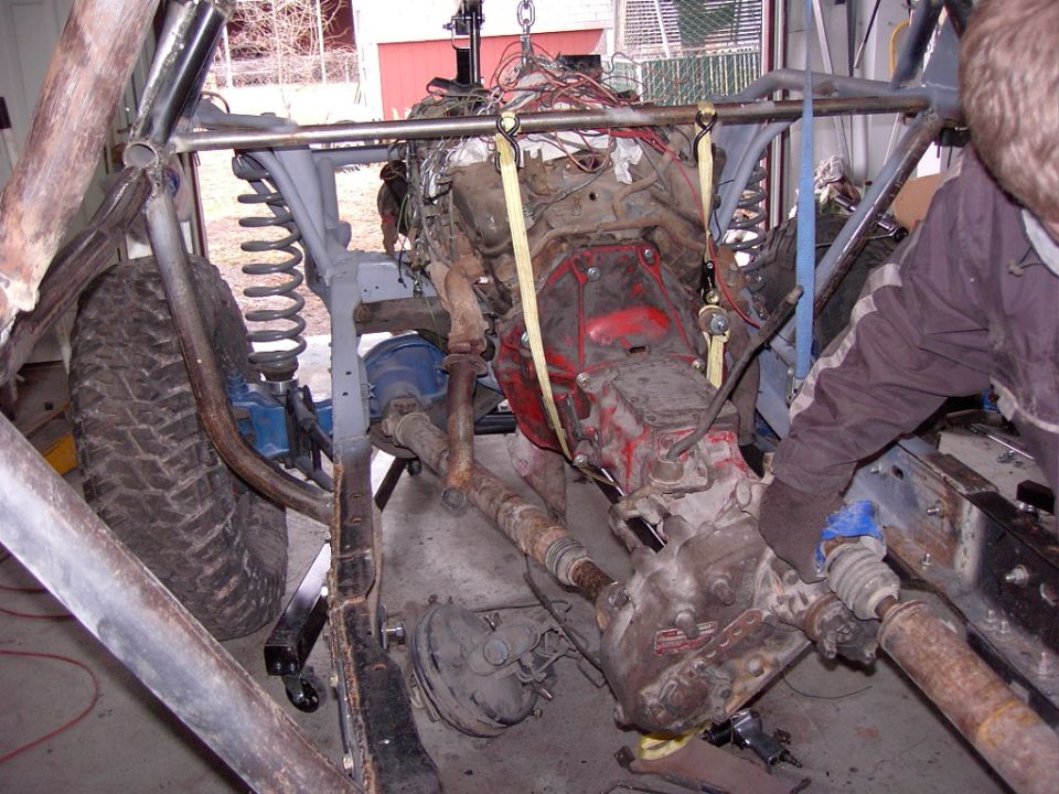 Engine and transmission assembly suspended by straps, with drivetrain components visible below