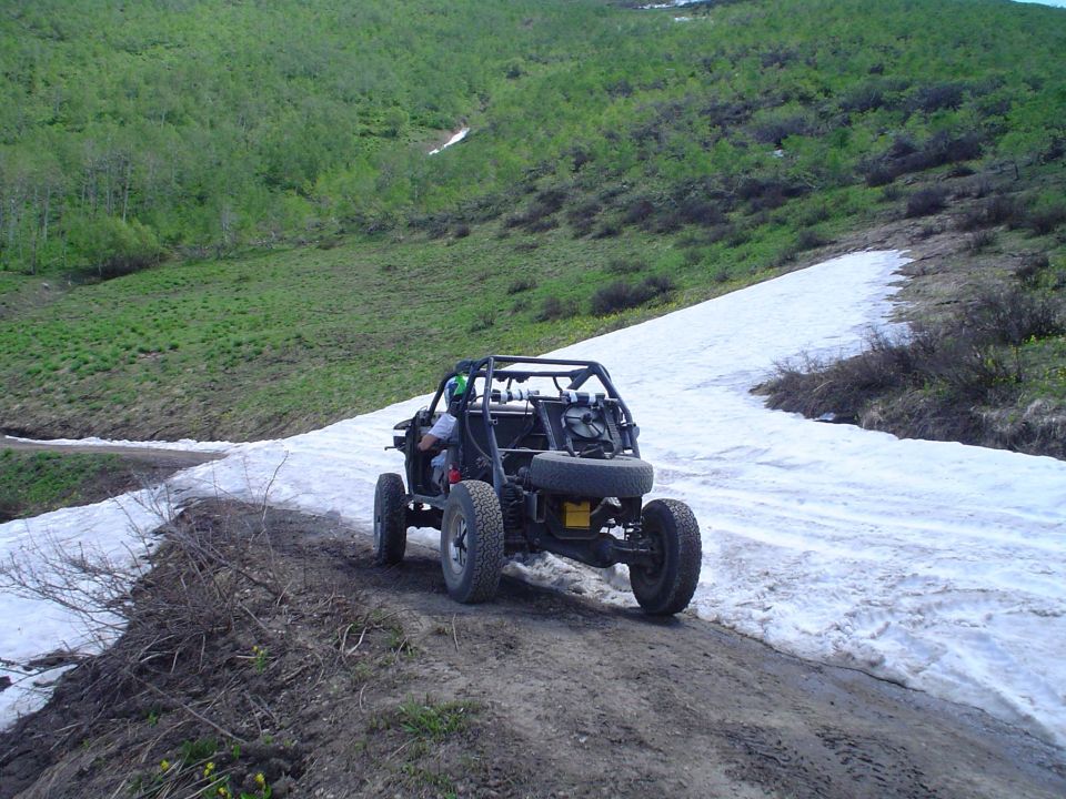 Off-road buggy driving on a dirt road with snow patches on the side, heading uphill