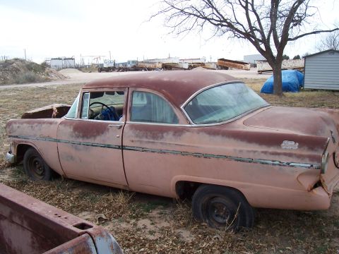 1955 Ford Customline - A weathered 1955 Ford Customline sits in a dry, outdoor lot, showing signs of age and disuse.
