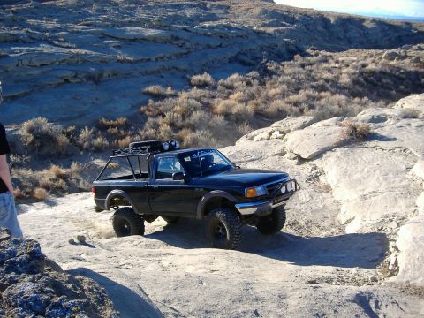 1978 Ford Bronco - A modified black pickup truck tackles a challenging rocky trail with a custom roof rack and bull bar.