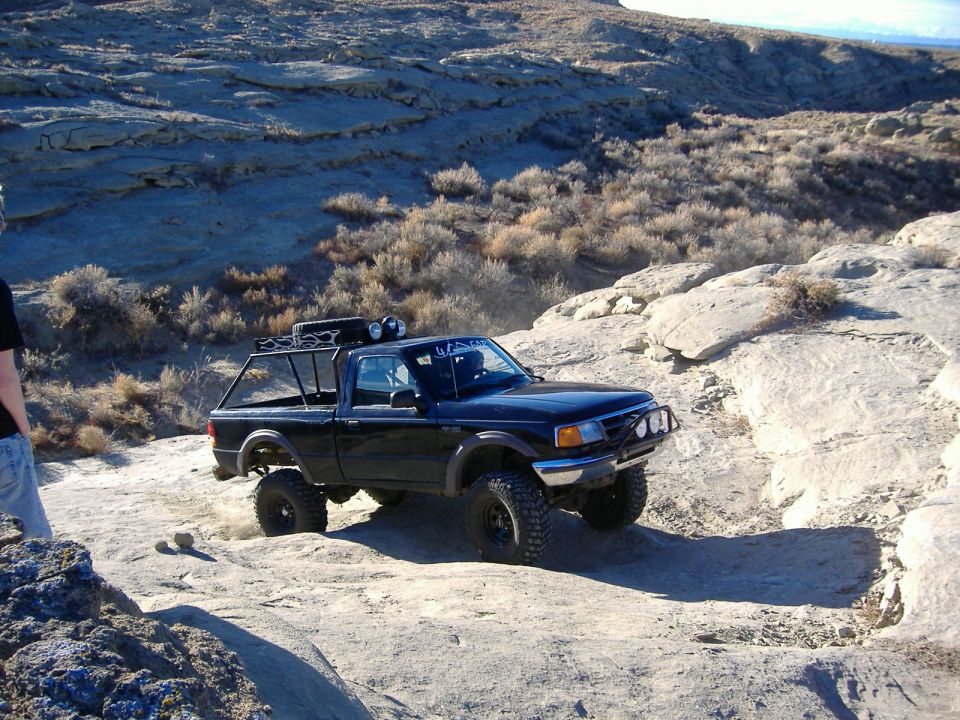 Black off-road pickup truck with roof rack and bull bar navigating rocky terrain