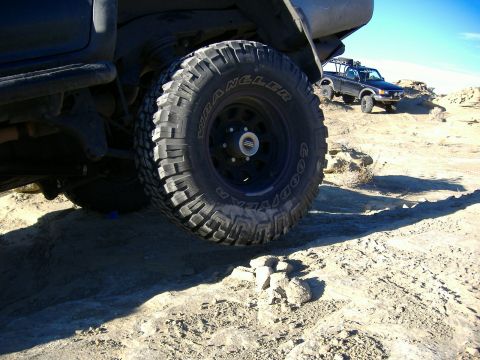 1978 Ford Bronco - Two off-road trucks navigate a challenging dirt trail under a clear sky.