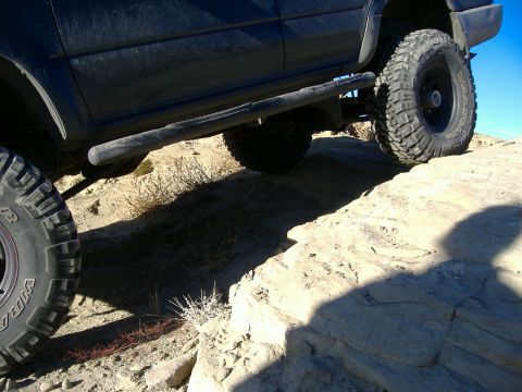 1978 Ford Bronco - A dark SUV navigates a rocky trail, its large tires gripping the uneven surface.
