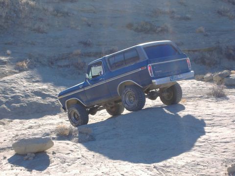 1978 Ford Bronco - A blue 1978 Ford Bronco navigates a challenging off-road trail with steep inclines and rocky terrain.