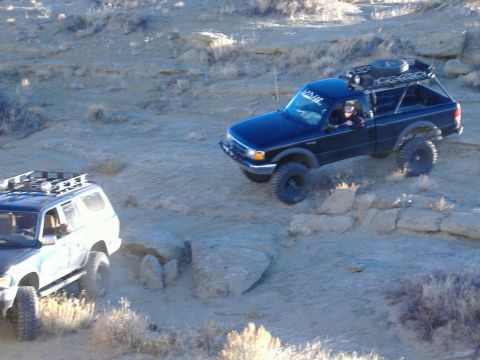 1978 Ford Bronco - Two off-road vehicles navigate a challenging rocky terrain under a clear sky.