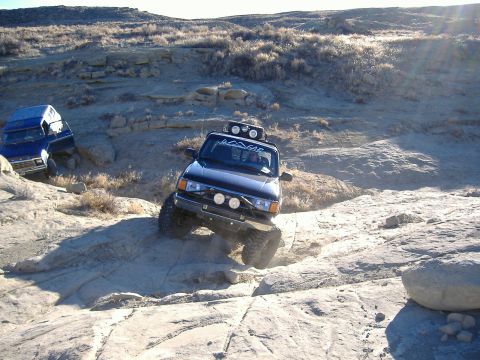 1978 Ford Bronco - Two modified off-road vehicles tackle a challenging rocky incline in a desert landscape.