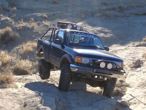 1978 Ford Bronco - A modified black pickup truck navigates a rocky terrain with its tires off the ground.