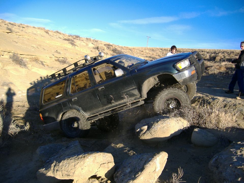 Dark green SUV with roof rack navigating rocky terrain, front passenger side wheel elevated