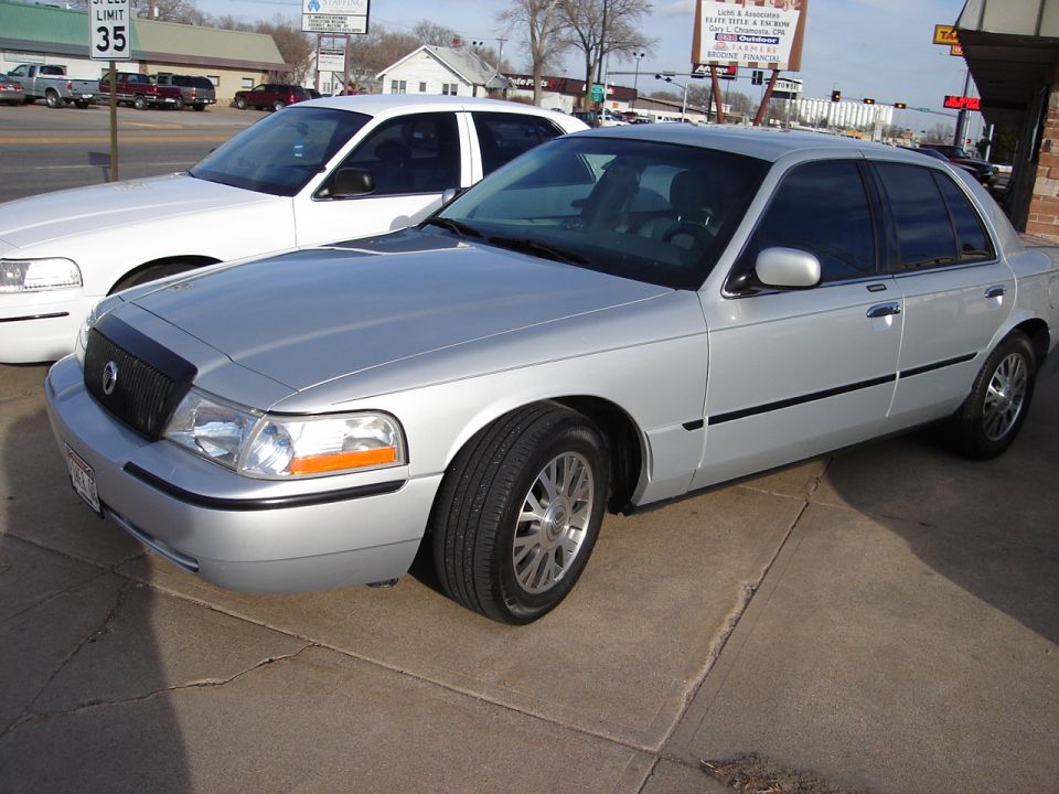 Silver 2000 Ford Crown Victoria parked on concrete, white sedan behind it