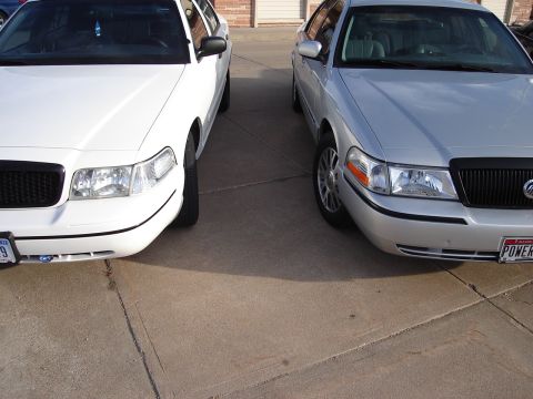 2000 Ford Crown Victoria - A white and a silver 2000 Ford Crown Victoria are parked next to each other, showing their front ends.