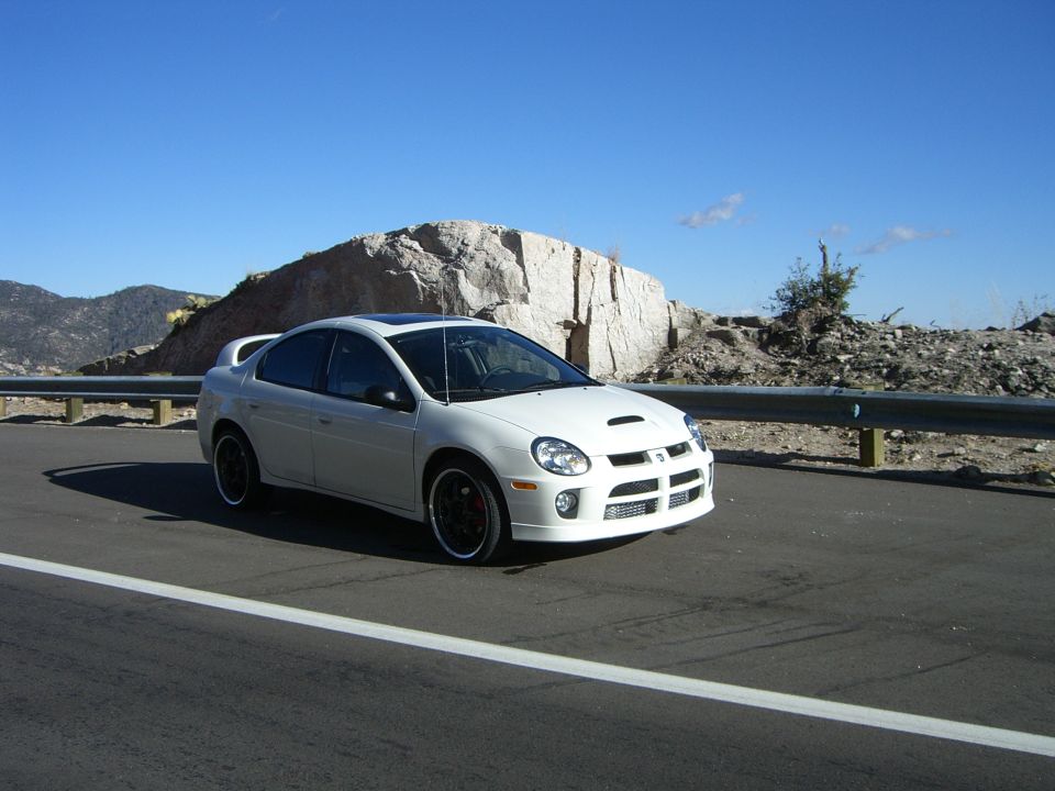 White Dodge Neon SRT-4 parked on the side of a road with a large rock formation in the background