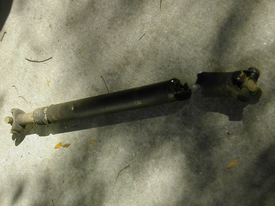 Disassembled driveshaft with U-joint yoke and slip yoke lying on a concrete floor