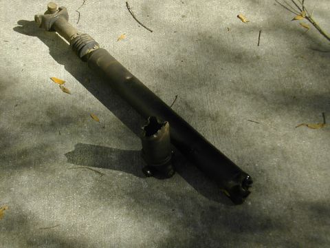 1993 Ford Bronco - A failed driveshaft lying on a concrete pad, its tube torn open and split at the end where the U-joint yoke ripped out, with the separated…