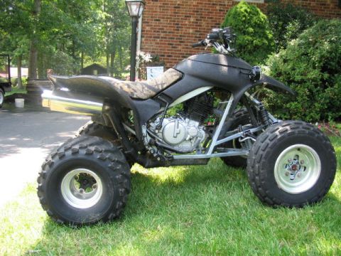 1987 Honda 250 X - This ATV is parked on grass in front of a brick house and trees.