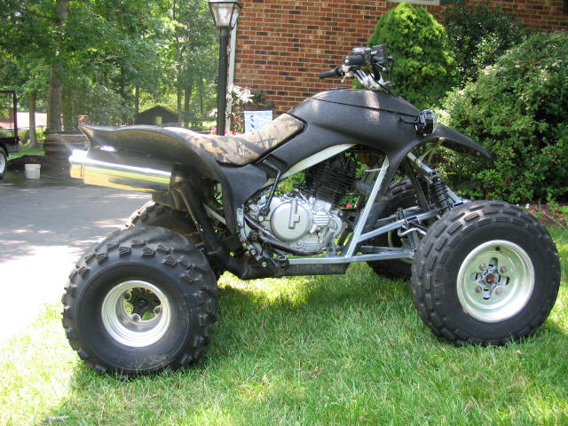 Black sport quad ATV in side view parked on grass with chrome exhaust and knobby tires