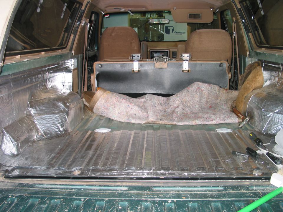 Rear cargo area of green Ford Bronco with foil insulation installed on floor, seat folded down, tools visible