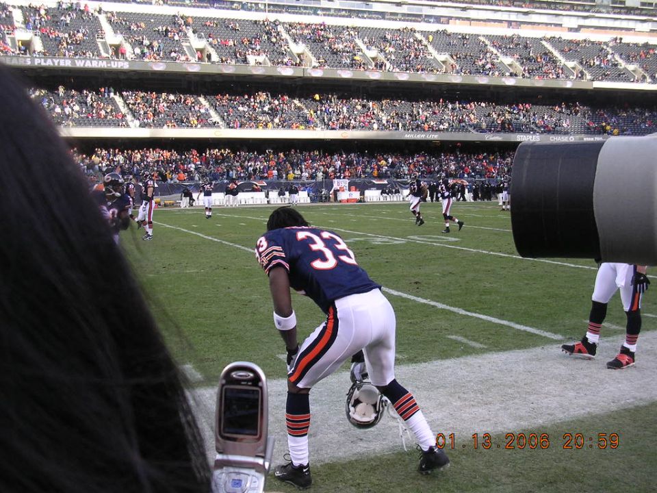 Football players on a field with stadium seating in the background. A flip phone is in the foreground