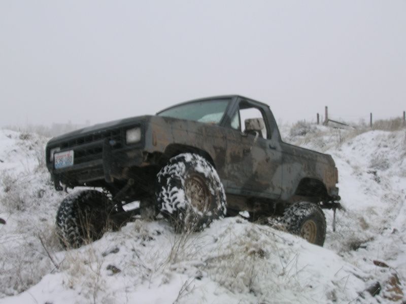 Muddy topless lifted Bronco II flexing on a snow-covered embankment