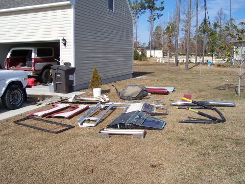 1978 Ford Bronco - Various parts from a 1978 Ford Bronco are spread across the lawn, with a Bronco visible in the garage.