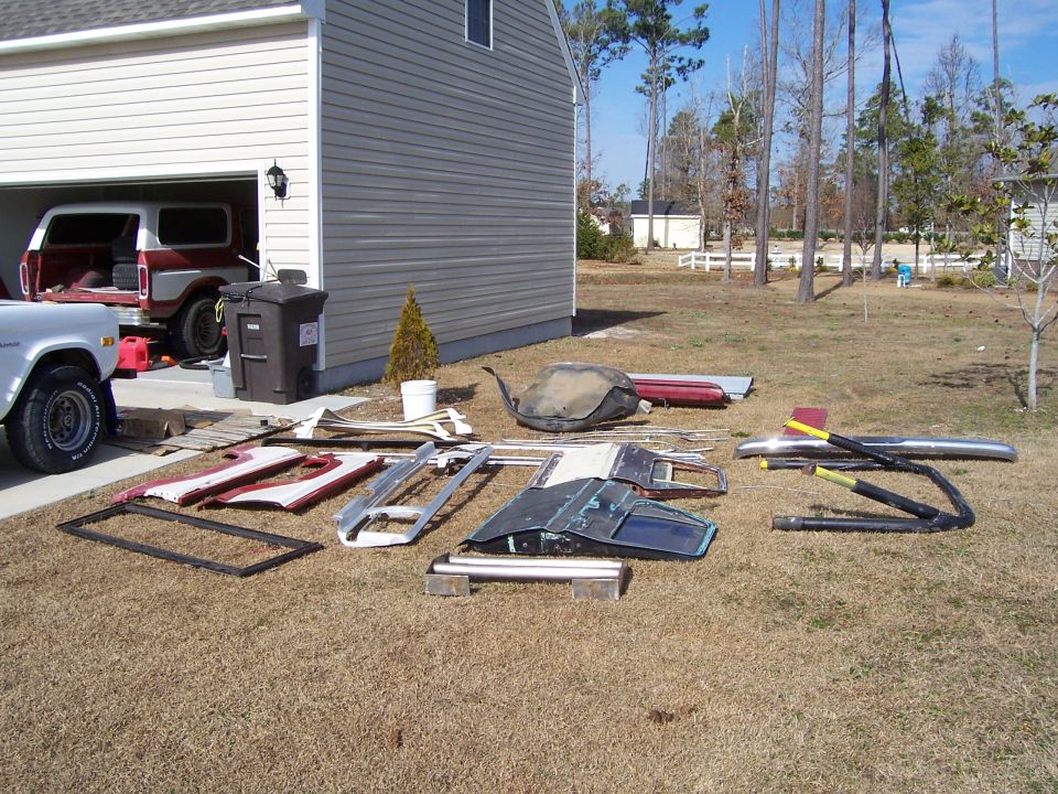 1978 Ford Bronco parts laid out on grass next to a white pickup truck and a Bronco in a garage