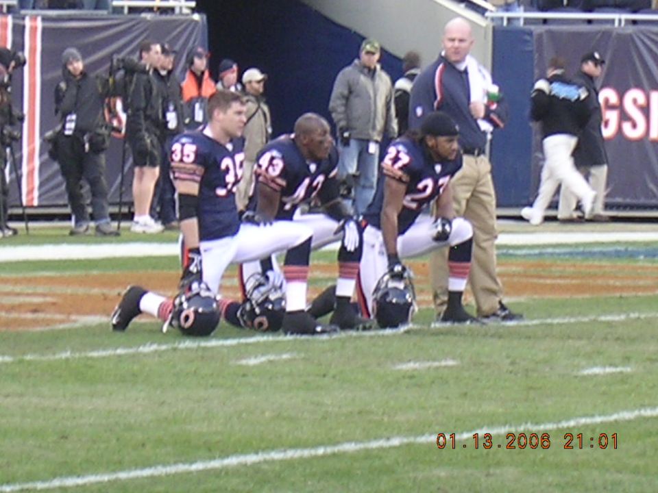 Football players in uniform kneeling on a field, with helmets on the ground. A date stamp reads 01.13.2008