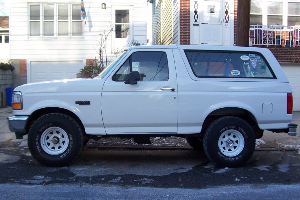 White Ford Bronco parked on street, side view. Has stickers on rear window
