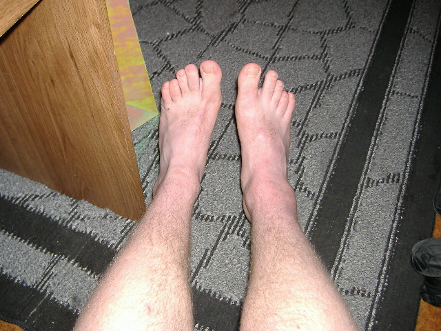 Human feet and legs standing on carpet next to wooden furniture