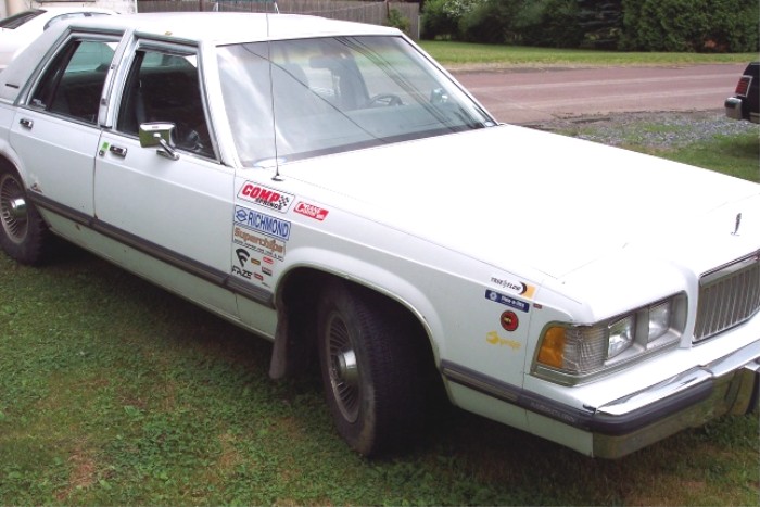 White sedan with various racing stickers on the doors and fender. It has a chrome grille and square headlights