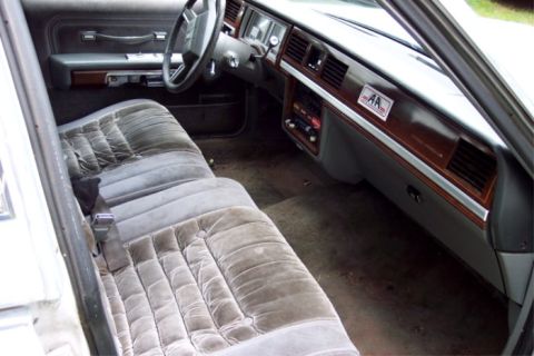 1988 Mercury Grand Marquis - The interior of a 1988 Mercury Grand Marquis shows plush velour seating and a wood-grain dashboard with an 'AA' license plate frame.