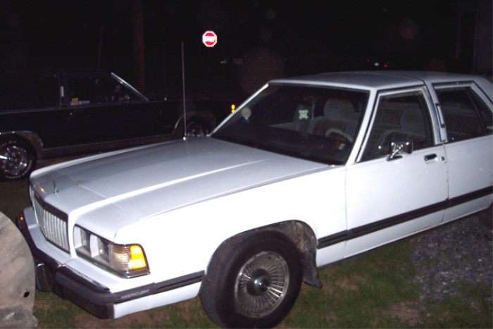 White Mercury sedan at night, front three-quarter view with wire wheel covers