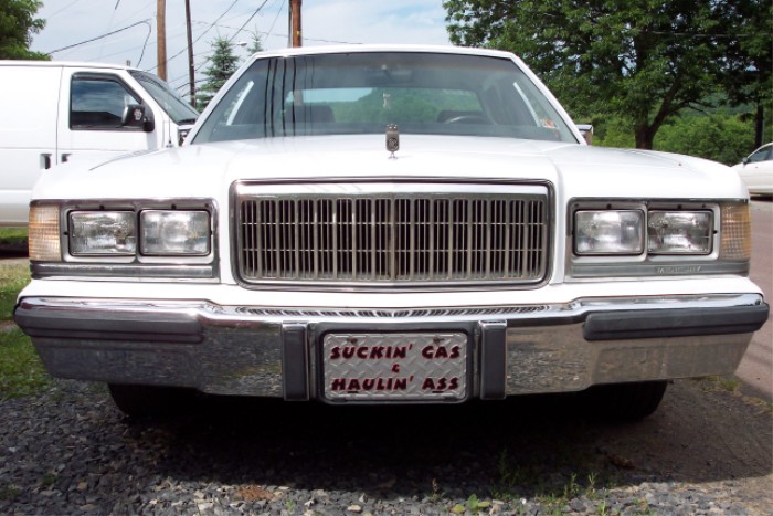 White 1988 Mercury Grand Marquis with a custom license plate that says 'Suckin Gas & Haulin Ass'