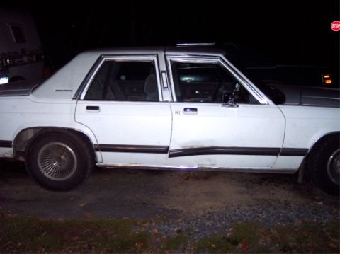 1988 Mercury Grand Marquis - A white sedan with a dented door and chrome trim is parked outdoors at night.