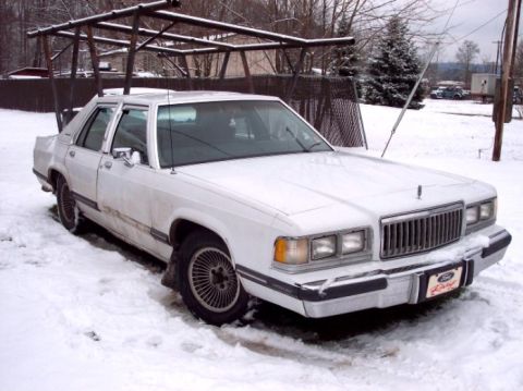 1988 Mercury Grand Marquis - A white 1988 Mercury Grand Marquis sits in the snow, its front grille and headlights clearly visible.