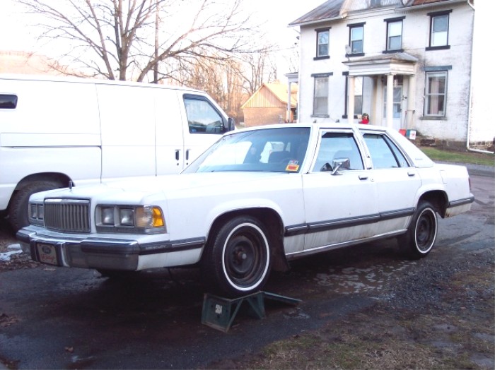 White Mercury Grand Marquis sedan, front 3/4 view, front end raised on a stand