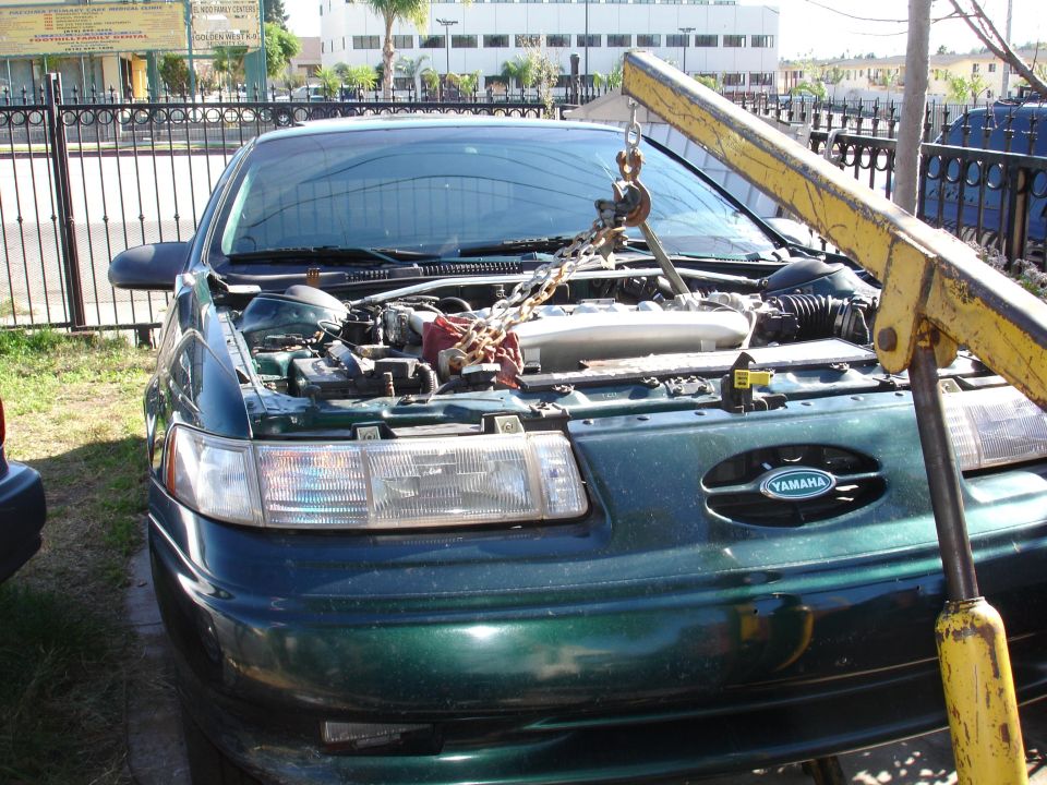 1993 Ford Taurus front view, hood open, engine being lifted by a yellow engine hoist