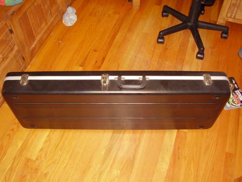 1996 Ford F-150 - A black guitar case rests on a polished wooden floor next to a chair and some stickers.