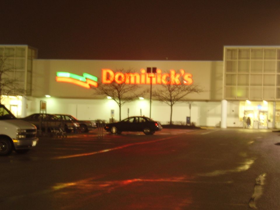 Dominick's grocery store storefront lit at night with cars in a wet parking lot