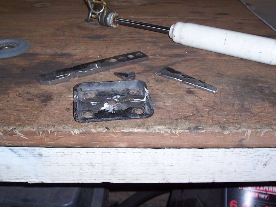 Metal bracket with four bolt holes and a shock absorber on a wooden surface