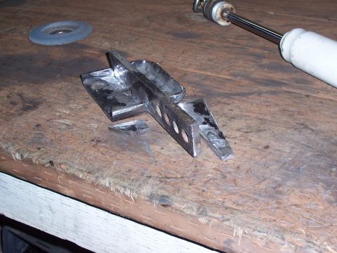 1988 Suzuki Samurai - A fabricated metal bracket with multiple holes sits on a workbench next to a shock absorber and grinding disc.