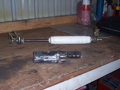 1988 Suzuki Samurai - A white shock absorber and a black metal bracket are displayed on a wooden workbench.
