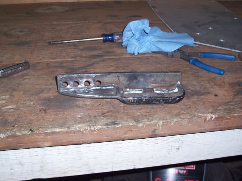 1988 Suzuki Samurai - A metal bracket with holes and welded supports sits on a workbench next to tools.