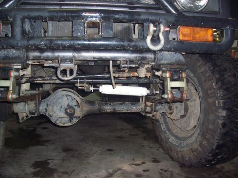 1988 Suzuki Samurai - Close-up view of the front axle, suspension, and off-road tires of a modified vehicle.