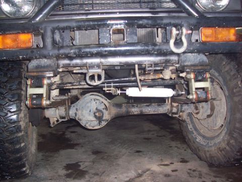 1988 Suzuki Samurai - Front axle and suspension components of a 1988 Suzuki Samurai, showing leaf springs and a steering stabilizer.