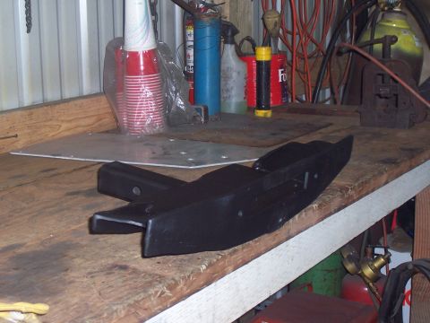 1988 Suzuki Samurai - A black metal part, possibly a hitch receiver, rests on a cluttered workbench.