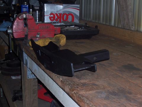 1988 Suzuki Samurai - A black metal part, possibly a hitch receiver, rests on a wooden workbench next to a red vise.
