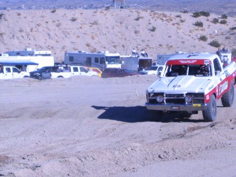 1990 Ford Bronco - white and red off-road race truck numbered 308 drives a sandy dirt track past the RV pit area.