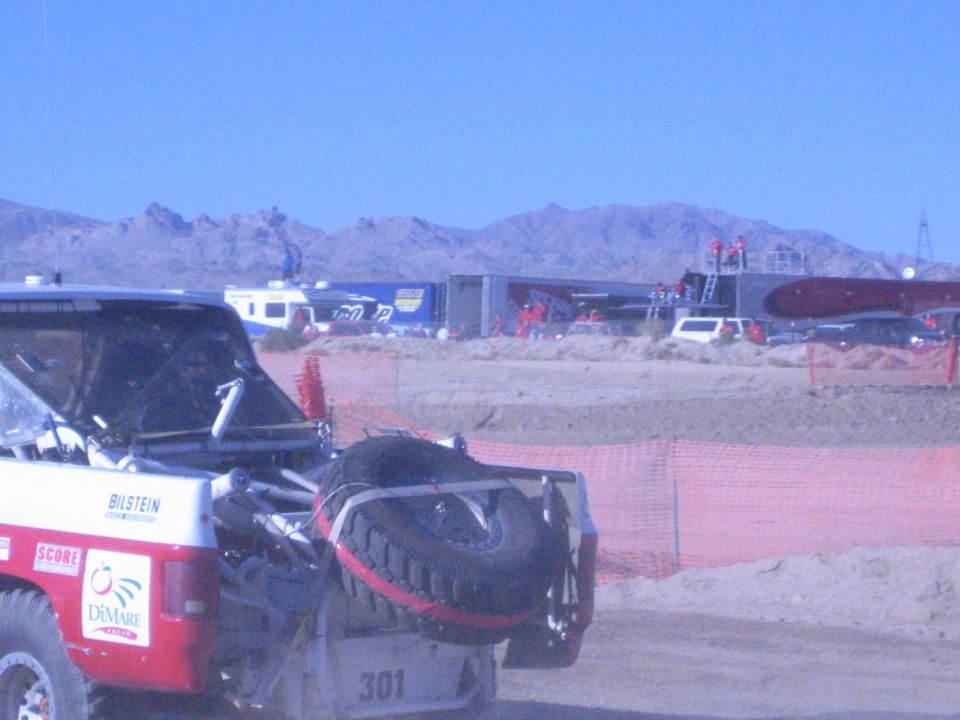 Rear of a number 301 race truck with spare tire behind orange fencing, desert mountains and pits behind