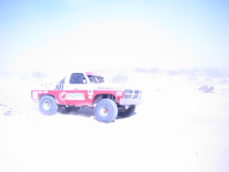 Red and white number 301 off-road truck driving through bright dusty desert terrain